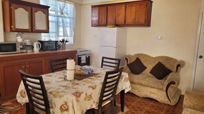 Una cocina compacta con armarios de madera, una mesa de comedor con sillas, un refrigerador y un sofá.