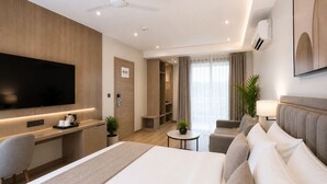 Ein Hotelzimmer mit einem großen Bett, einem Schreibtisch mit Flachbildfernseher, einer Sitzecke mit Sofa und Sesseln, einem kleinen Tisch und einer Pflanze.