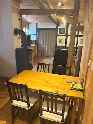 A wooden dining table with four chairs, a black stove, and a wooden floor. - Vacation apartment in 200-year-old Winningen winegrower's house (Winningen)