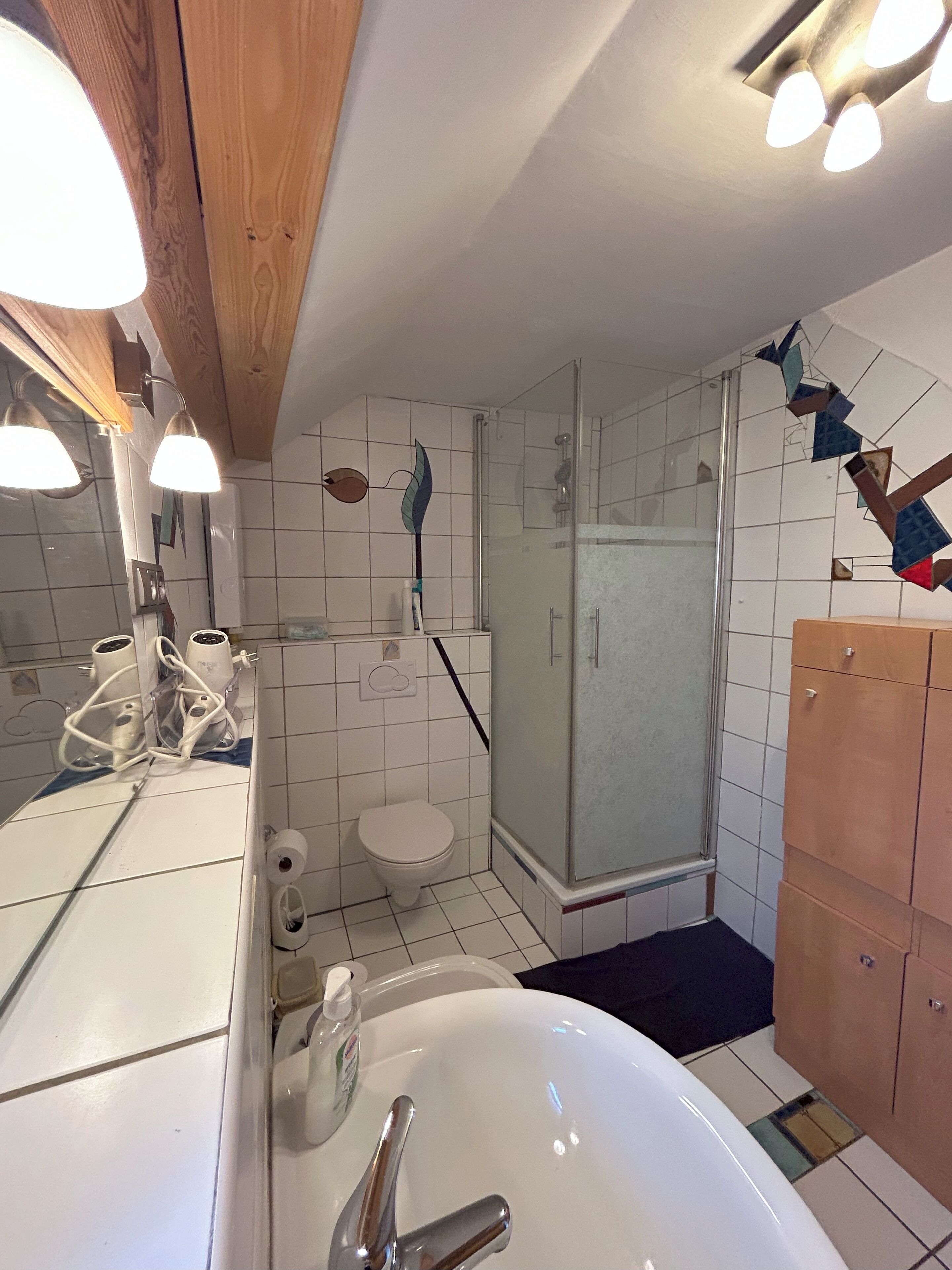 Et badeværelse med en hvid vask, toilet og en bruseniche med glasvægge.
