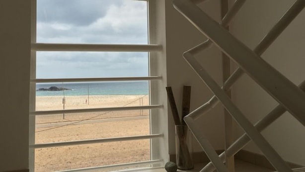 Quarto com uma grande janela com vista para a praia, uma escadaria e piso de azulejos.