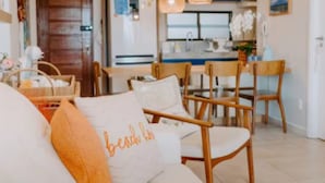Ein gemütliches Wohnzimmer mit einer Couch, einem Essbereich mit Holzsesseln und einer Küche im Hintergrund.