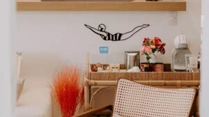 Ein Zimmer mit einem weißen Sofa, einem Korbstuhl, einem an der Wand befestigten Regal mit Dekorationen und einem gerahmten Kunstwerk, das einen Schwimmer zeigt.