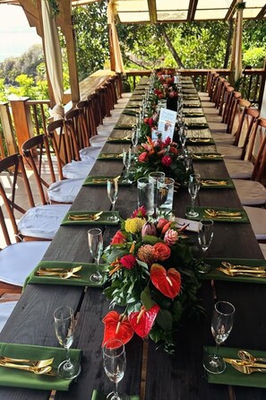 Une longue table à manger, dressée avec des sets de table verts, des couverts dorés et un centre de table floral.