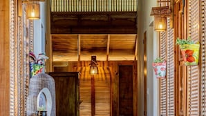 Un pasillo de madera con un interior rústico, que incluye un banco de madera, plantas en macetas y una pared decorativa con listones verticales.