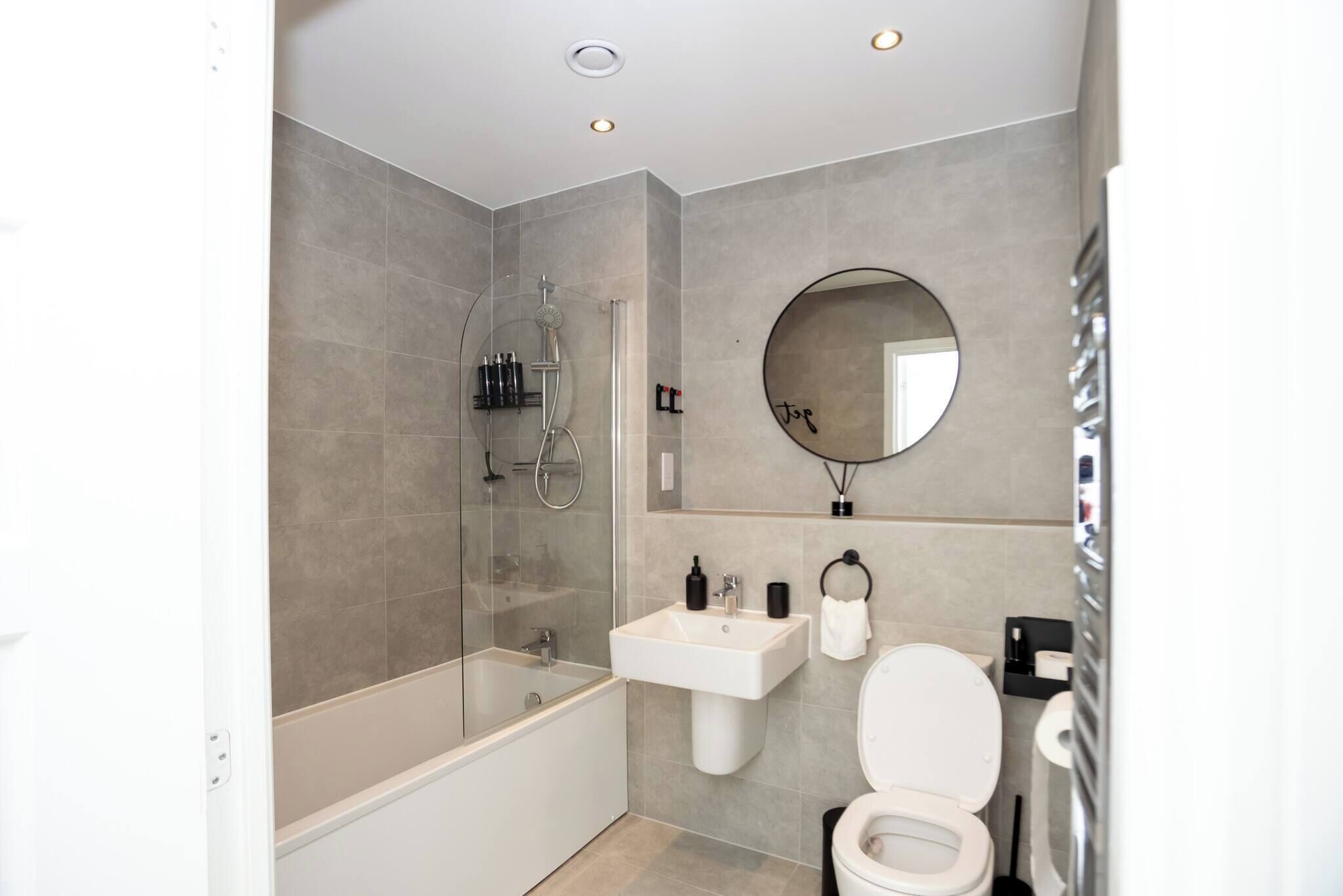 Een moderne badkamer met een badkuip, wastafel, toilet en een ronde spiegel.
