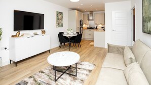 A modern living room with a flat-screen TV, a dining area with a table and chairs, a sofa, and a kitchen in the background. - The Prime Stay Free Parking EV Charger (Sittingbourne)