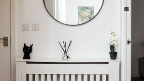 A white console with a round mirror above it, a small black sculpture, a potted orchid, and a decorative item on the console. - The Prime Stay Free Parking EV Charger (Sittingbourne)