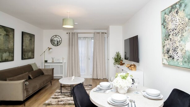 A modern living room with a sofa, a dining table set for four, and a TV mounted on the wall. - The Prime Stay Free Parking EV Charger (Sittingbourne)