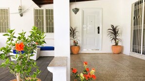 Un espace extérieur abrité, agrémenté de plantes en pot et doté d’une porte blanche.