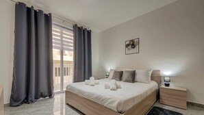 Une chambre d’hôtel avec un grand lit, une table de chevet, une petite table, une œuvre d’art accrochée au mur et une porte-fenêtre coulissante avec des rideaux.