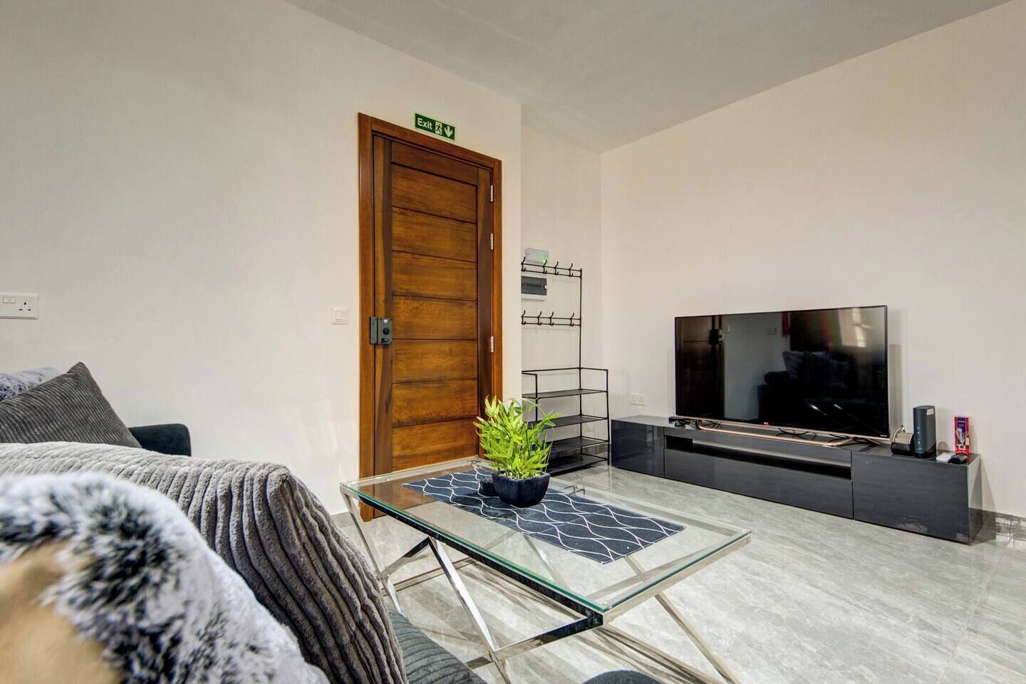 Una sala de estar moderna con una mesa de centro de vidrio, un televisor de pantalla plana, una puerta de madera y una pequeña planta sobre la mesa.