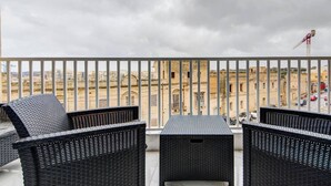Un balcon doté de meubles en osier et offrant une vue sur des bâtiments historiques.