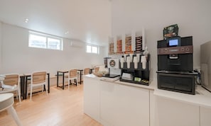 Un área de cocina moderna con cafetera, microondas y refrigerador. Hay sillas y una mesa en la zona de comedor.