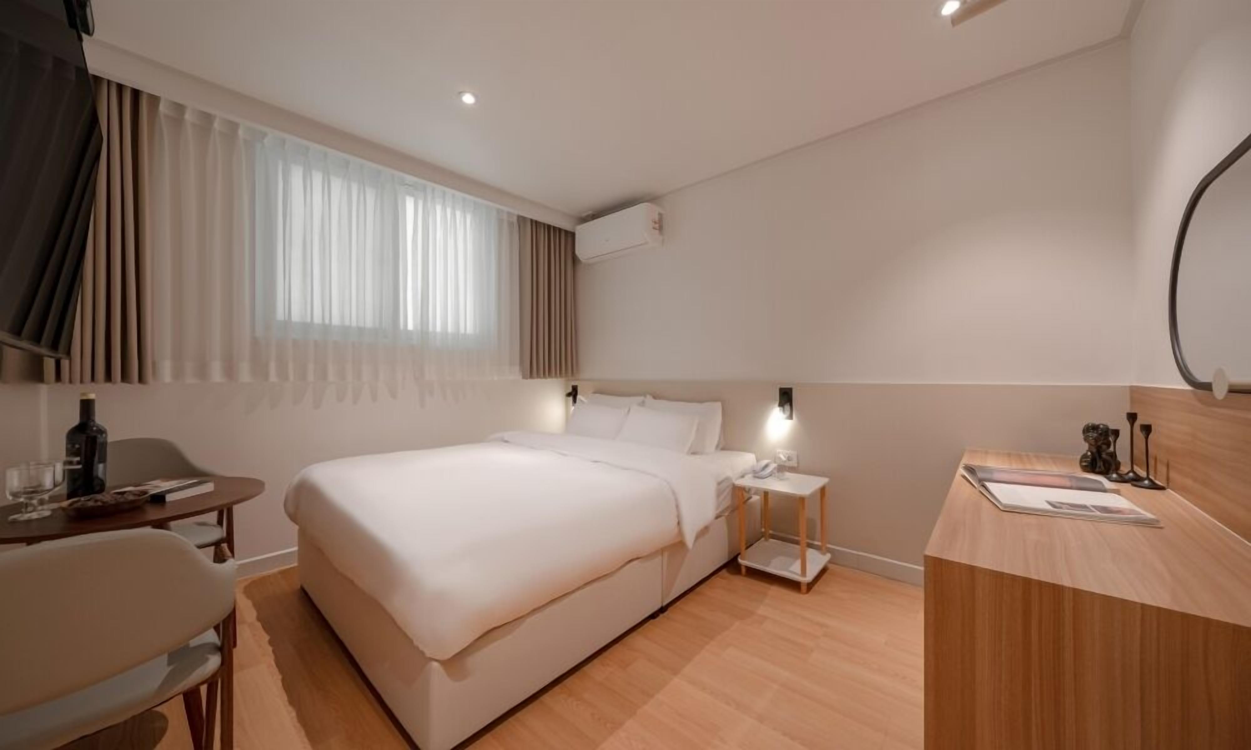 Habitación de hotel con cama, mesita de noche, escritorio, silla y una ventana con cortinas.