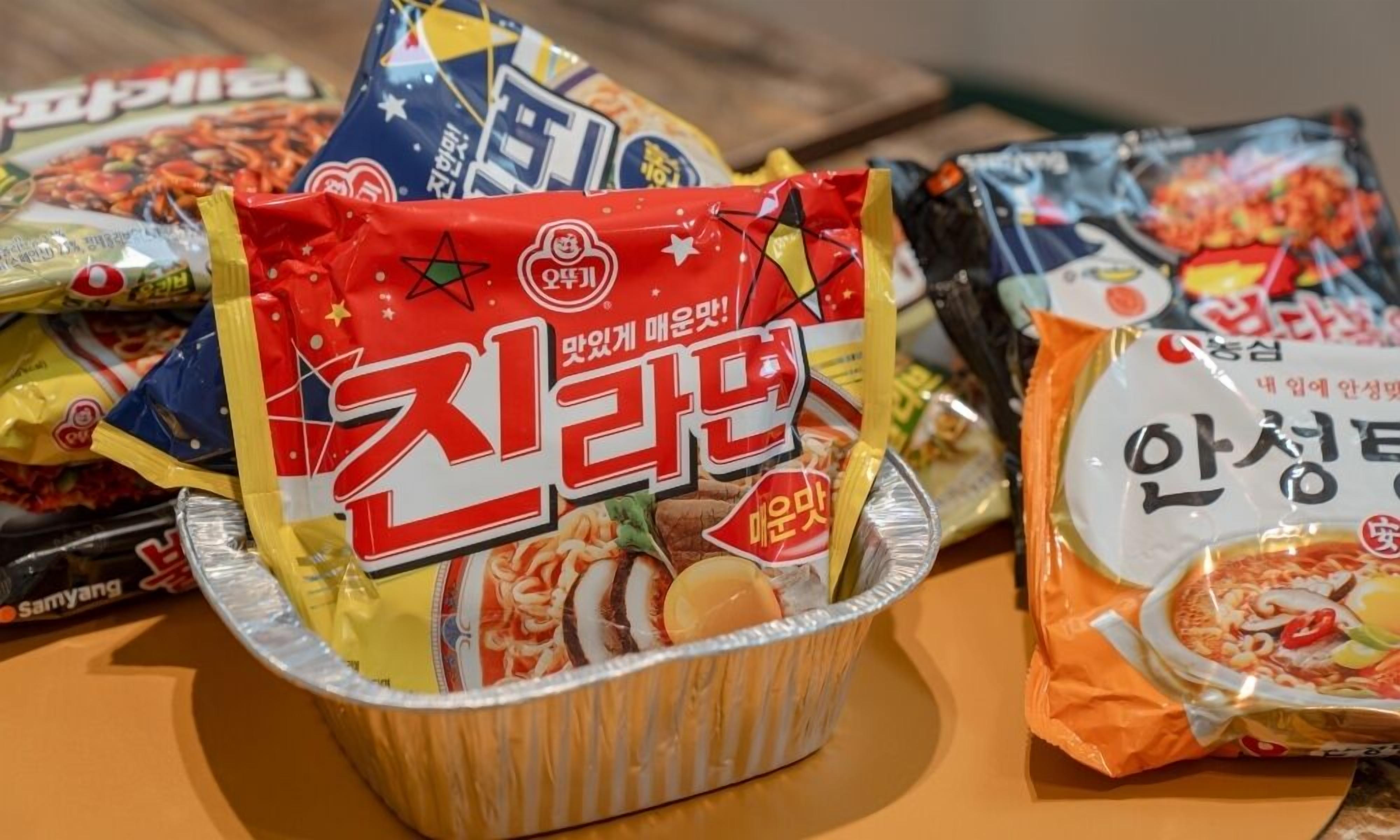 A variety of packaged food items, including instant noodles and snacks, displayed on a table.