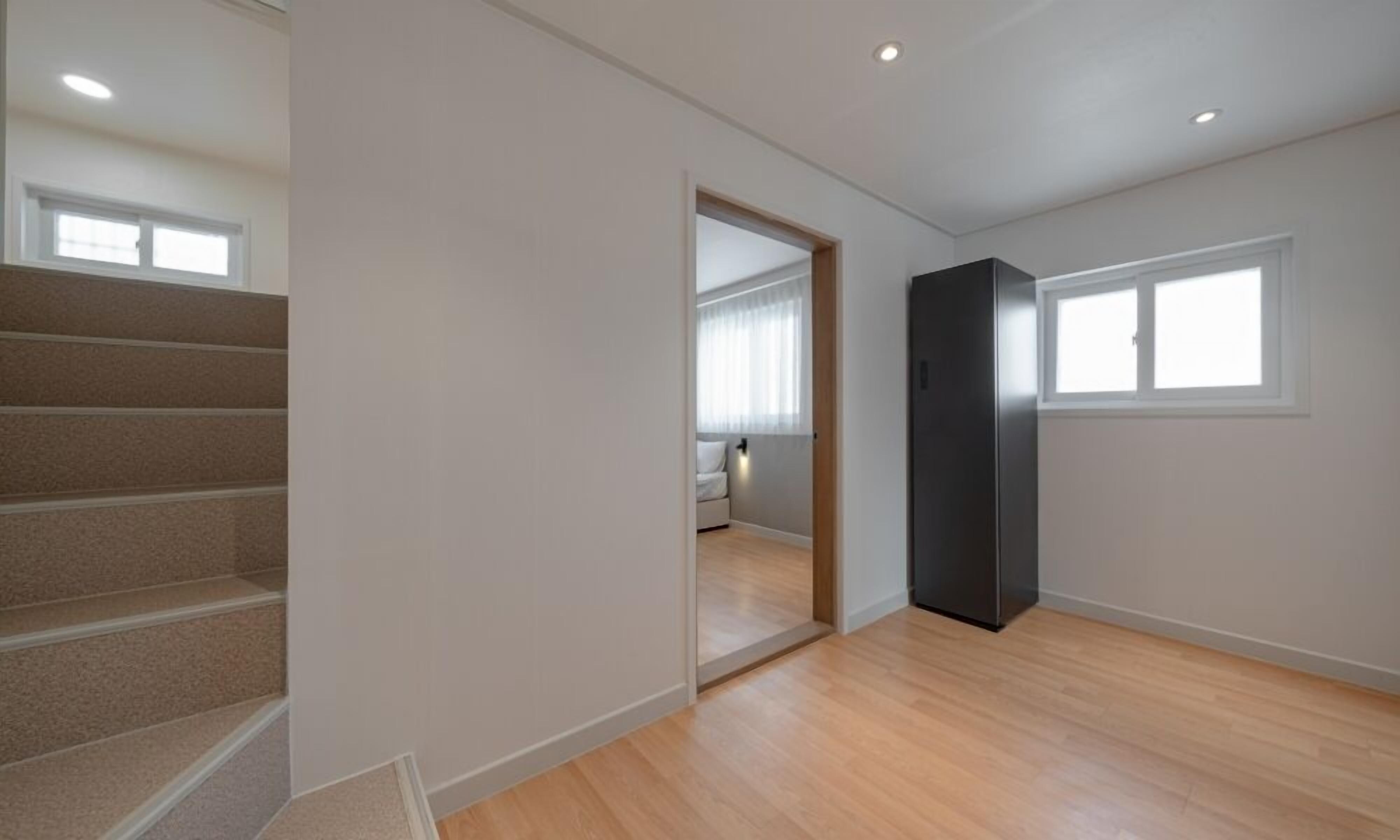 Una habitación con una escalera, una puerta que da a otra estancia y una ventana.