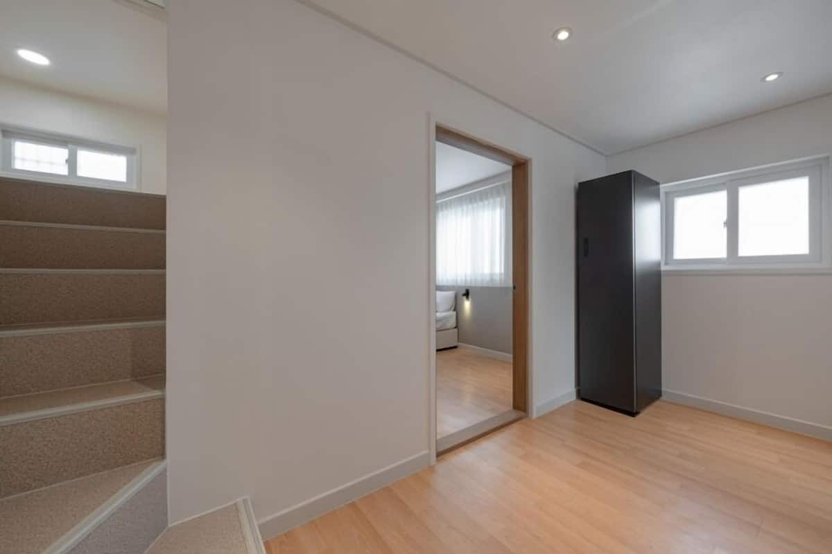 Una habitación con una escalera, una puerta que da a otra estancia y una ventana.