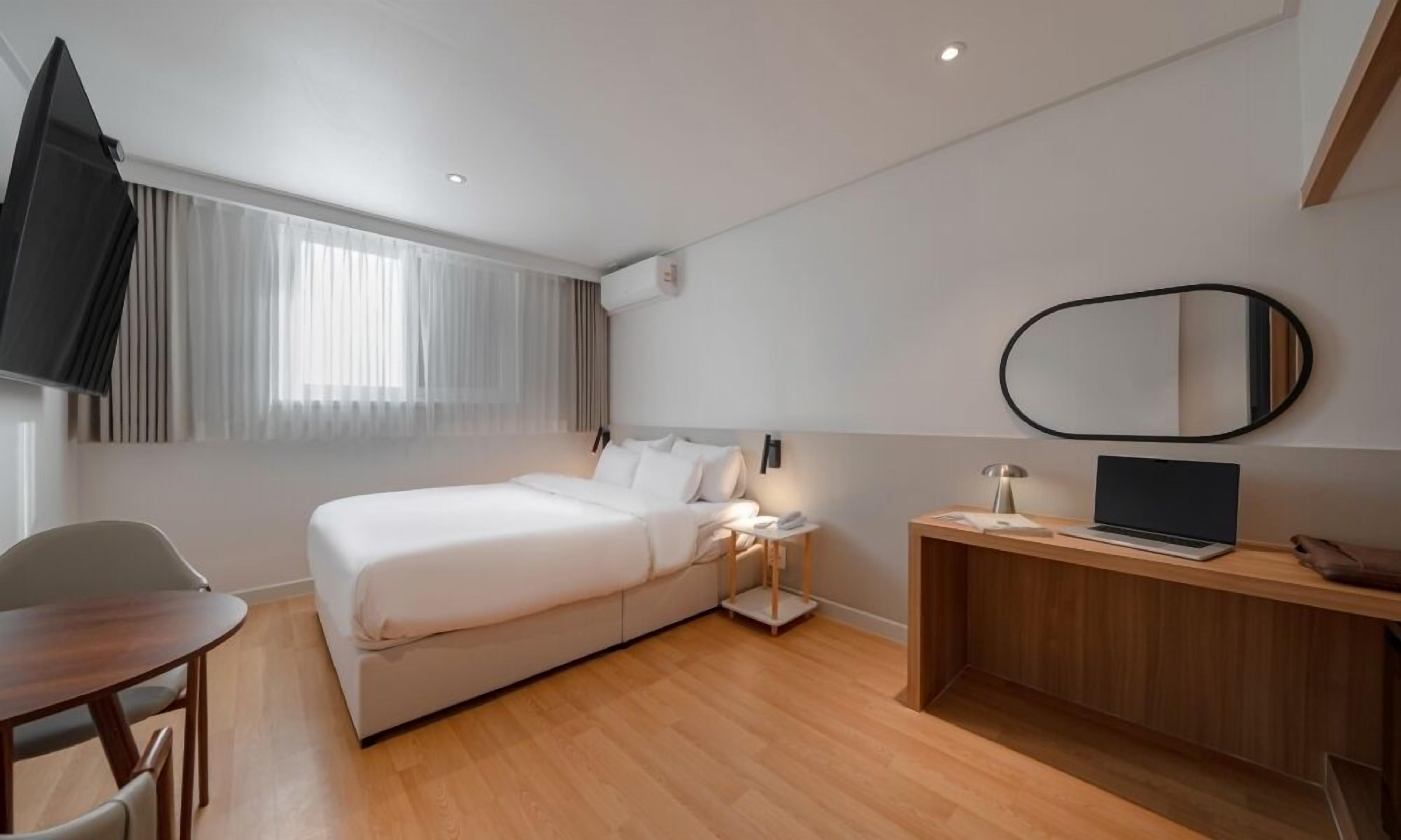 Habitación de hotel moderna con cama, escritorio, silla, televisor y espejo.