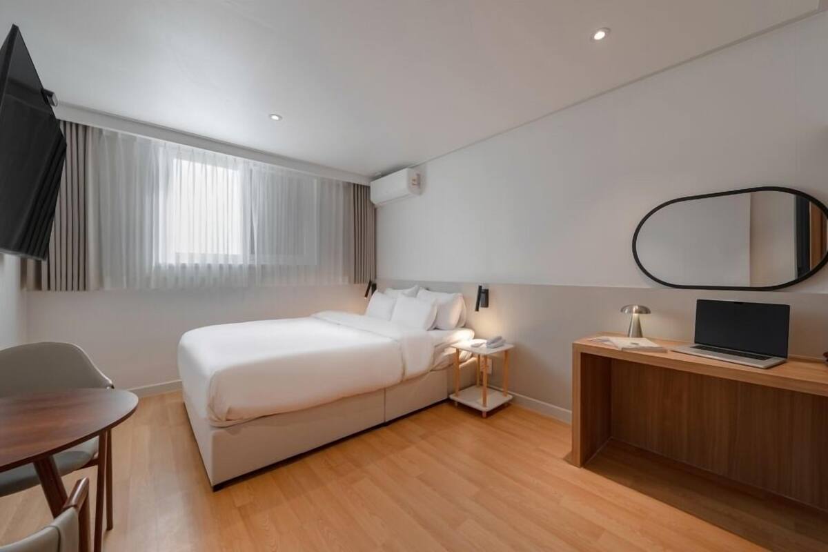 A modern hotel room with a bed, a desk, a chair, a TV, and a mirror.