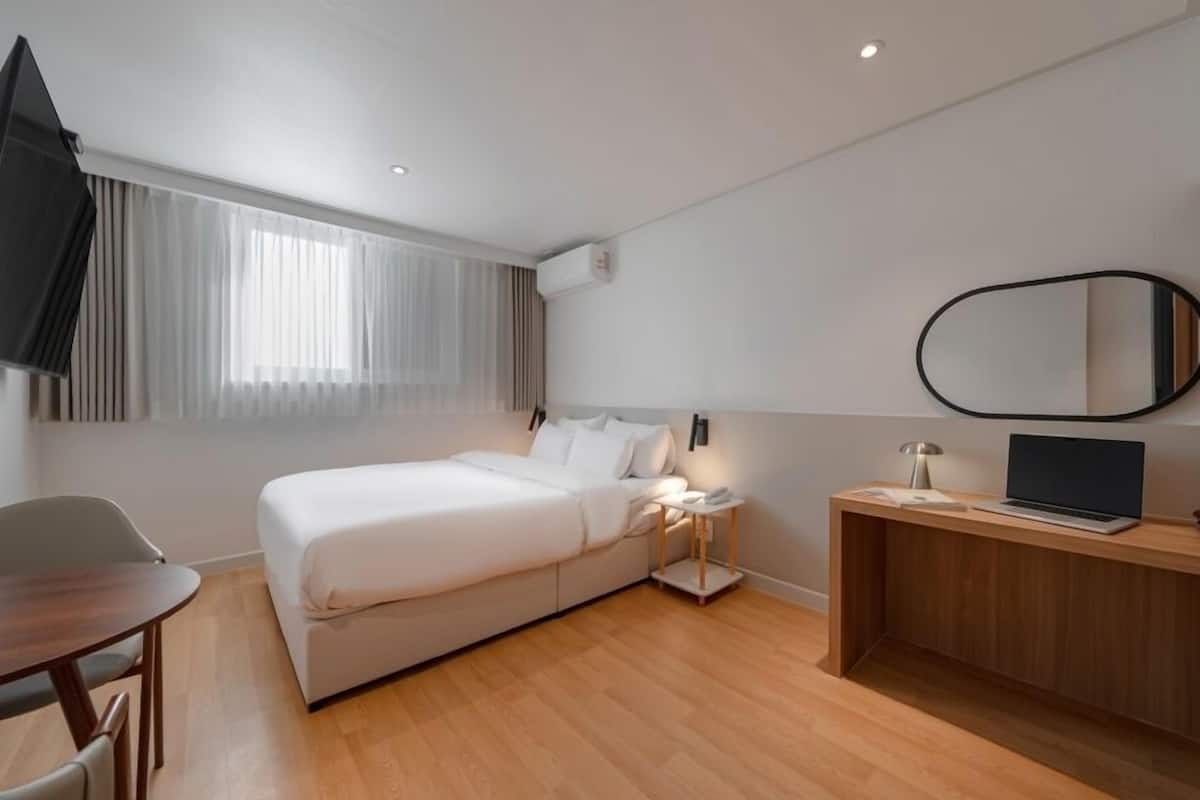 Habitación de hotel moderna con cama, escritorio, silla, televisor y espejo.
