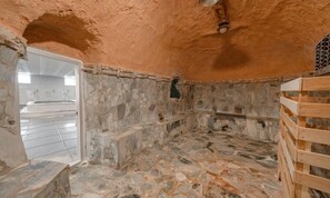 A stone-walled room with a wooden bench, a stone floor, and a view through an archway to a tiled area. - H Avenue Hotel Andong Culture Street (Andong)