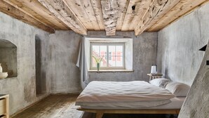 A bedroom with a wooden ceiling, a single bed, a small table with a lamp, and a window with a view of buildings. - Hofstätte 37 by Interhome (Vaduz)