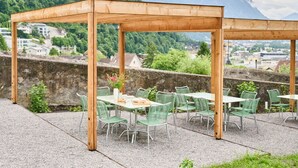 An outdoor patio with wooden pergola, green metal chairs, and tables, overlooking a mountainous landscape with a castle in the background. - Hofstätte 37 by Interhome (Vaduz)