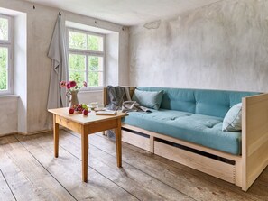 Une pièce chaleureuse avec un canapé de couleur turquoise, une table en bois ornée d’un vase de fleurs et une fenêtre avec des rideaux.