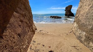 Ein Strand mit einer Felsformation in der Ferne, aufgenommen durch einen natürlichen Felsenbogen.