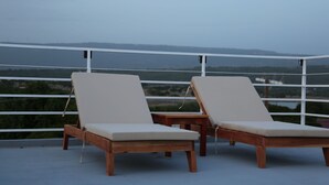 Two wooden lounge chairs with beige cushions on a balcony with a white railing, overlooking a landscape with greenery and distant buildings. - VillaMerissa schmiegt sich zwischen zwei unberührte Strände by Interhome (Belleair)