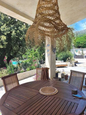 A round wooden table with chairs, a woven hanging light fixture, and potted plants.
