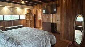 Ein Zimmer aus Holz mit einem Bett, einem Fernseher, einem Schminktisch und einem Spiegel.