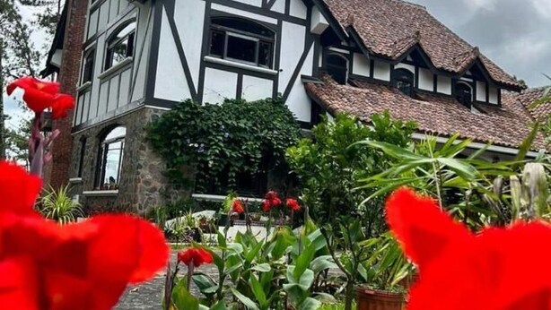 Ein traditionelles Haus im Tudor-Stil mit einem steilen Dach, weißem und schwarzem Fachwerk und einem Ziegelkamin.