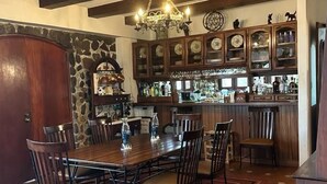Ein Essbereich mit einem großen Holztisch und Stühlen, einer Wand mit Steinverkleidung sowie eine Bar mit Schränken und einer Pendelleuchte.