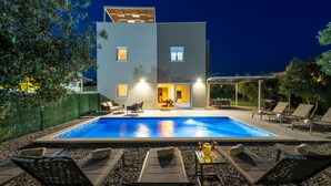 Una casa moderna de dos pisos con piscina, mobiliario exterior y un patio cubierto.