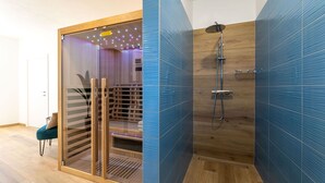 Un baño moderno con ducha, suelo de madera y una puerta de cristal que da a una zona de estar.