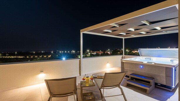Terraza en la azotea con jacuzzi, dos sillones y una mesa con bebidas.