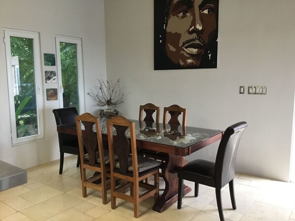 A dining area with a wooden table and chairs, a decorative plant, and a large painting on the wall.