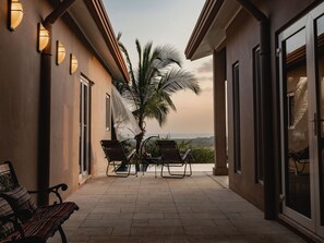 Une terrasse couverte avec deux chaises longues, un banc et un palmier.