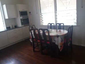 A dining area with a round table and six chairs, a kitchen area with cabinets and appliances, and a window with blinds. - Sulda's Home, eine Oase im Südwesten von Paramaribo by Interhome (Paramaribo)