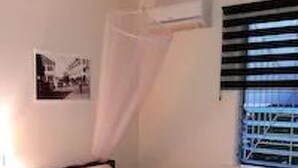 Una cama individual con colcha y almohadas blancas, una mesita de noche y un aire acondicionado de pared.