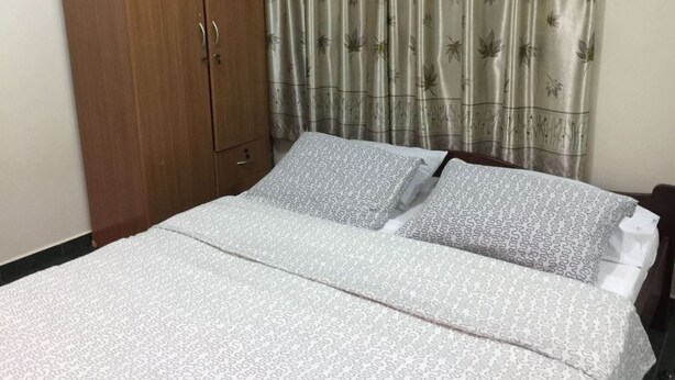 Un dormitorio con cama, armario de madera y cortina estampada con hojas.