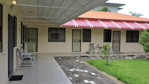 Un edificio con un patio empedrado, una zona cubierta con techo rojo y un pequeño jardín.