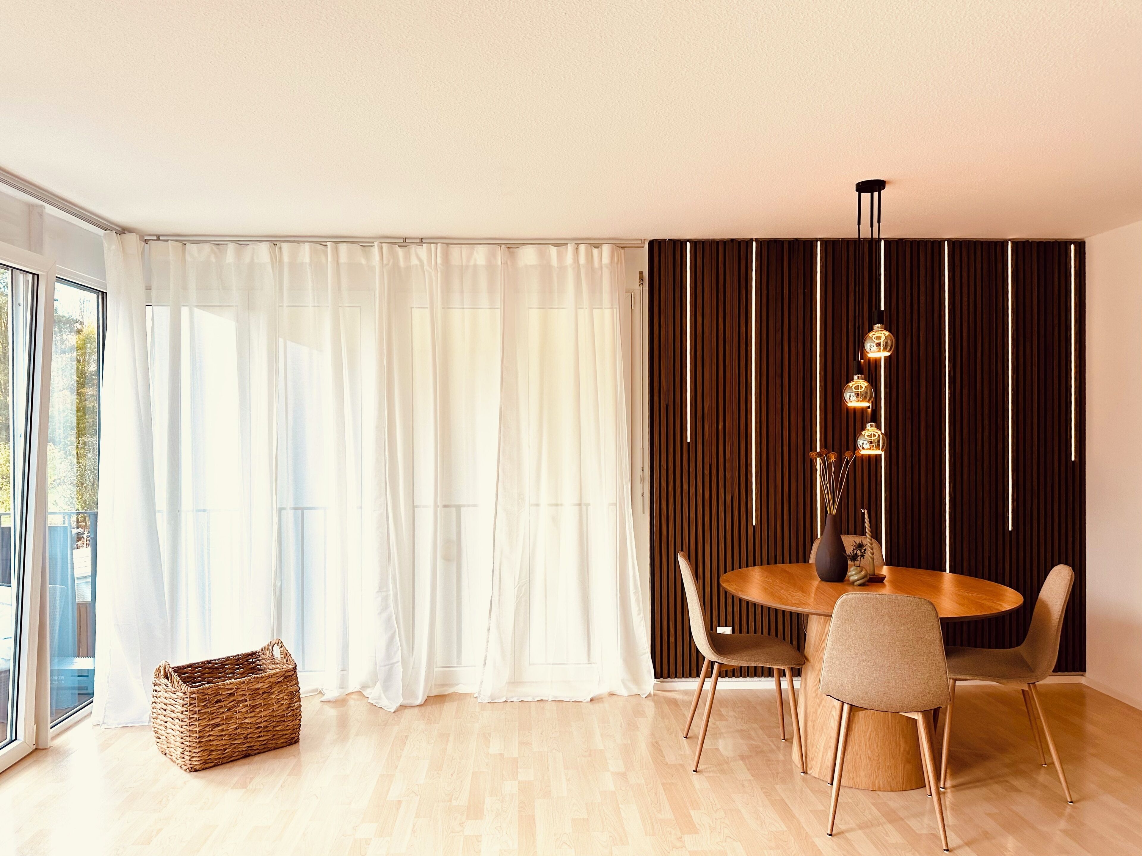 Een moderne eetruimte met een ronde houten tafel, vier stoelen en een hanglamp.