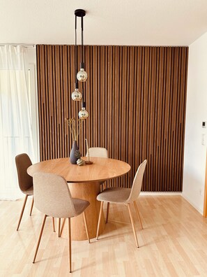 Un comedor moderno con una mesa redonda de madera, cuatro sillas y una lámpara colgante.