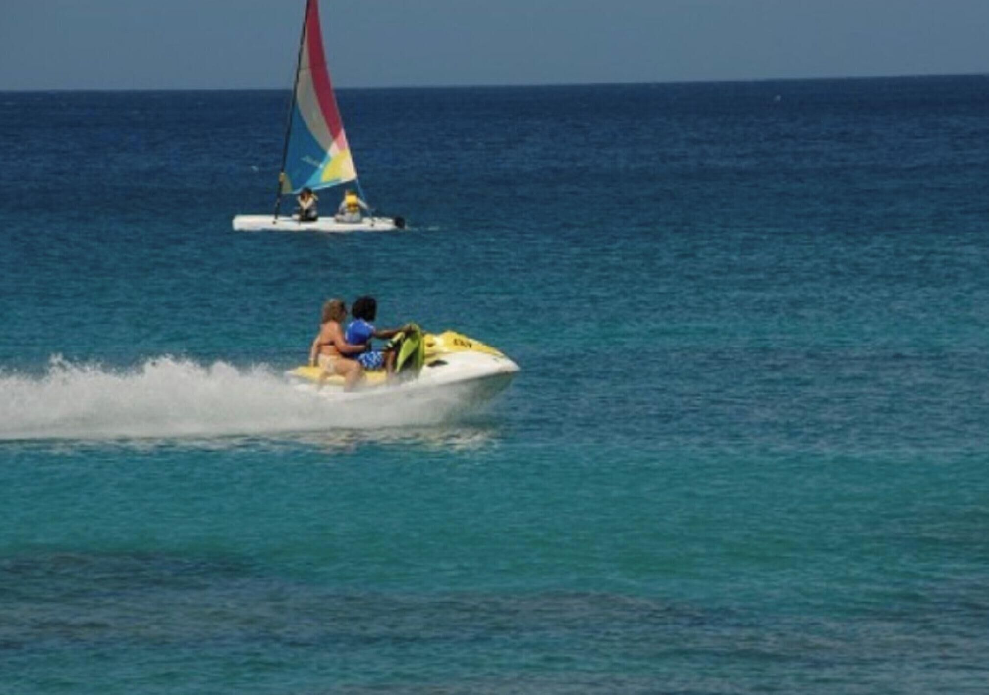 A jet ski on a calm sea with a sailboat in the background.