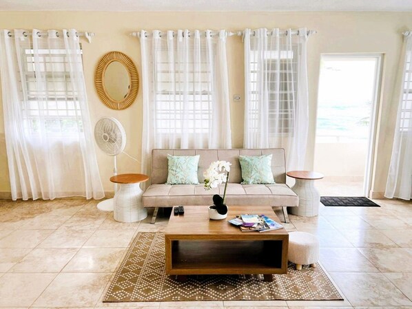 Un salon avec un canapé beige, deux tables d’appoint, une table basse et un tapis à motifs.
