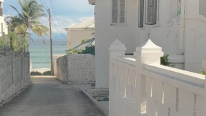 A narrow street with a white building on the right, a white fence, and a view of the ocean. - Gelassenes "Island Escape" mit Meerblick by Interhome (Christ Church)