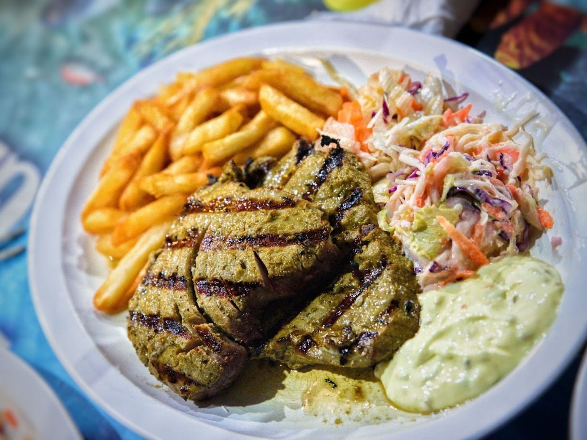 A plate with grilled meat, French fries, coleslaw, and a creamy sauce.